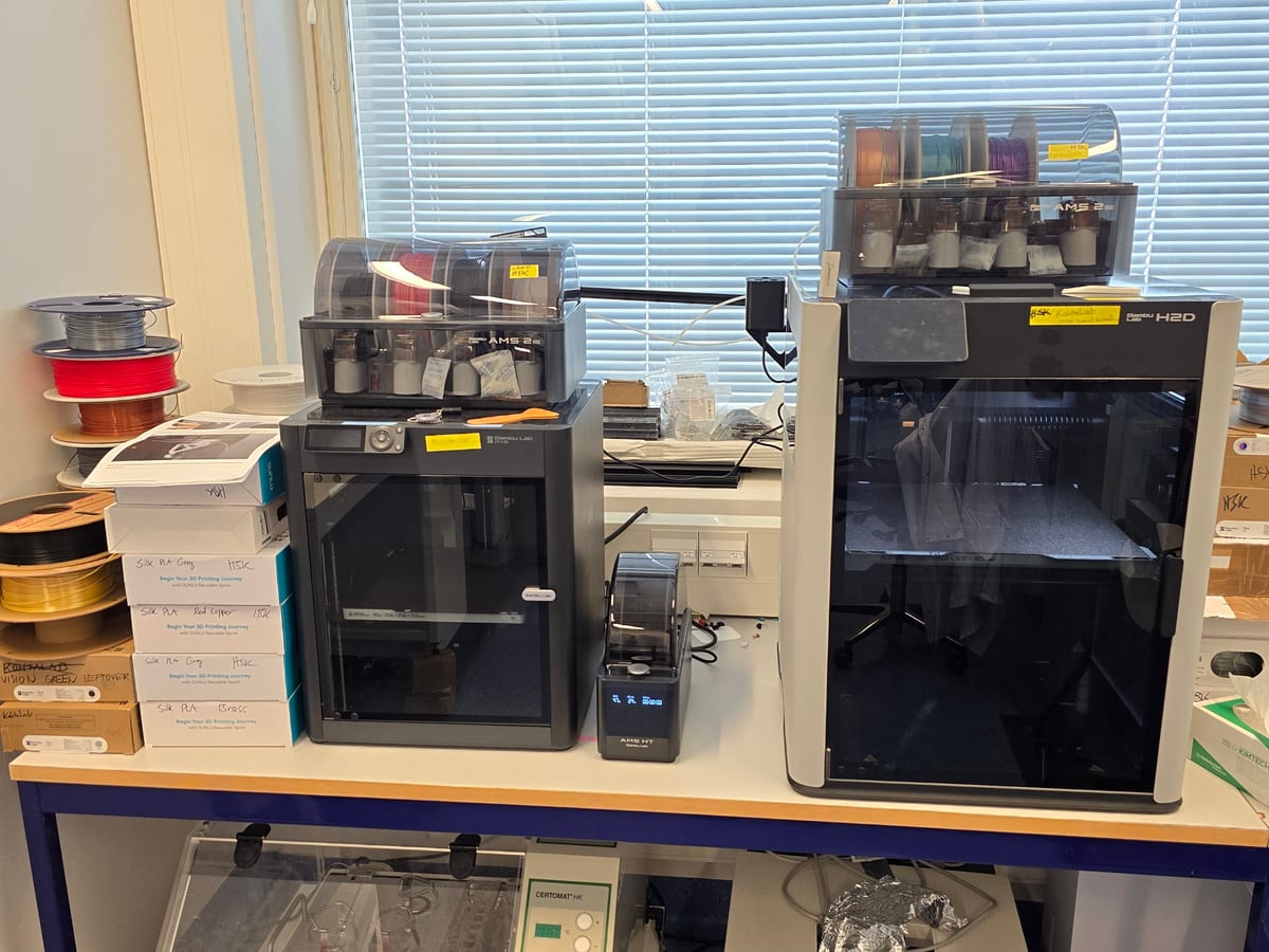 Two 3D printers with filament units on a lab bench
